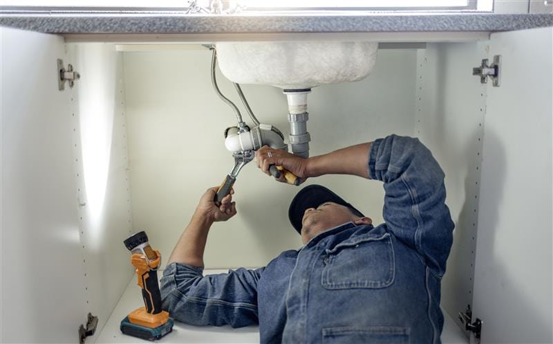 Plumber repairing pipes beneath a bathroom sink in Daly City